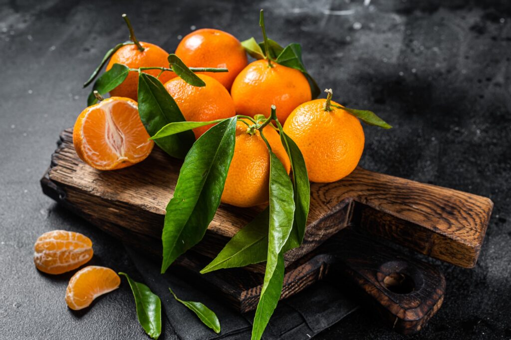 Mandarin oranges or tangerines fruits with leaves on wooden board. Black background. Top view